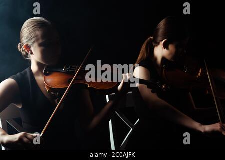 due musicisti che suonano musica classica sui violini sul palcoscenico scuro Foto Stock