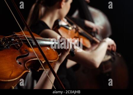 visione ritagliata di musicisti professionisti femminili che suonano su violini su palcoscenico scuro, fuoco selettivo Foto Stock