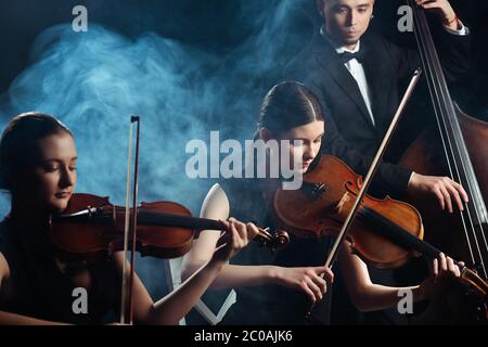 trio di musicisti che suonano su violini e contrabbassi su palcoscenico scuro con fumo Foto Stock