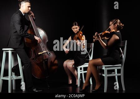 trio di musicisti professionisti che suonano su strumenti musicali su palcoscenico scuro Foto Stock