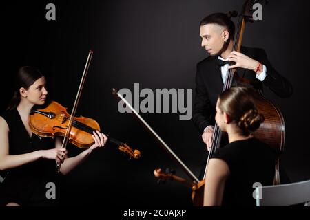 trio di musicisti professionisti che suonano su strumenti musicali su palcoscenico scuro Foto Stock