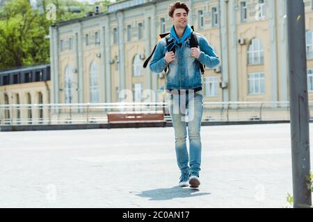 Fuoco selettivo di uomo di consegna sorridente con zaino termico che cammina sulla strada urbana Foto Stock