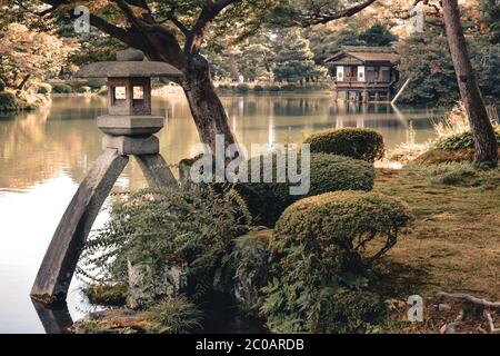 Lanterna di pietra e una casa sul lago nel giardino Kenrokuen a Kanazawa Giappone Foto Stock