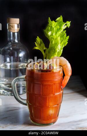 Cocktail di vodka Mary sanguinosa in una birra stein con guarnitura di gamberi su tavolo da cucina in marmo Foto Stock