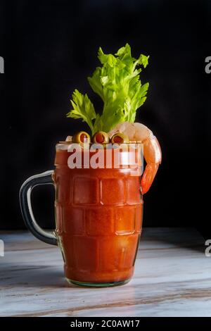 Cocktail di vodka Mary sanguinosa in una birra stein con guarnitura di gamberi su tavolo da cucina in marmo Foto Stock