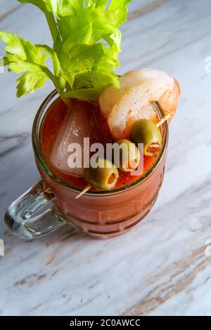 Cocktail di vodka Mary sanguinosa in una birra stein con guarnitura di gamberi su tavolo da cucina in marmo Foto Stock