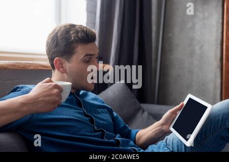 uomo sorpreso che tiene la coppa e guarda il tablet digitale con schermo vuoto Foto Stock