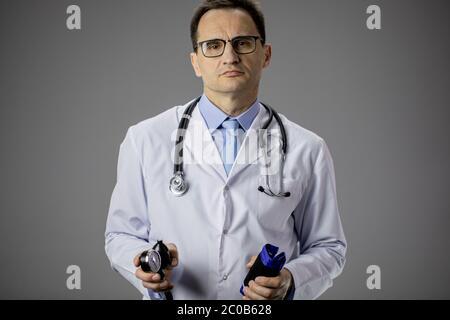 Serio medico anziano che tiene tonometro su fondo grigio, pressione sanguigna Foto Stock