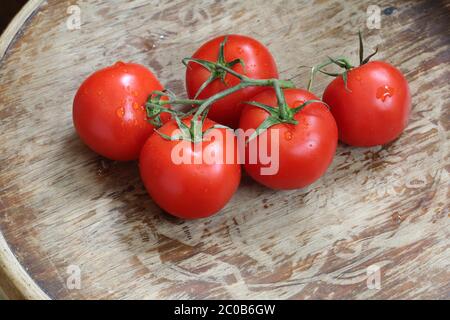 I pomodori rossi su un ramo verde giacciono su un tavolo di legno Foto Stock