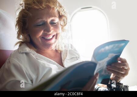 Rivista di lettura Donna matura su un aereo Foto Stock