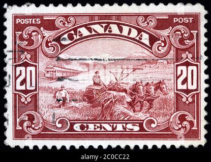 OTTAWA - CIRCA 1927: Francobollo canadese che mostra l'attrezzatura di coltivazione del grano vecchio stile trainata da cavalli, in Alberta con le Montagne Rocciose in Th Foto Stock