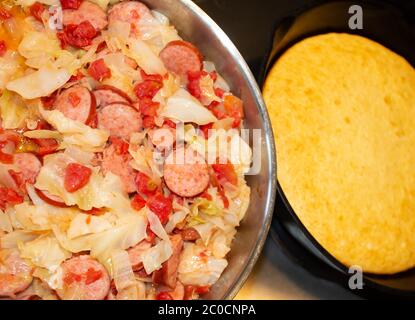 Cucina tipica del sud con cavolo fritto, salsiccia, cipolle e pomodori. Il pane di mais cotto in una padella di ferro si prepara a questo pasto facile da preparare Foto Stock