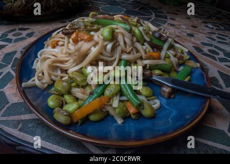Un piatto di pasta vegana con verdure come carote, fagioli verdi e edamame. Foto Stock