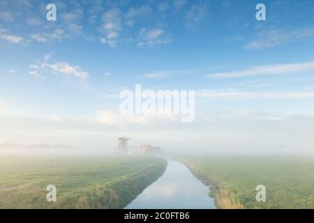 affascinante mulino a vento dal fiume in mattina nebbiosa Foto Stock