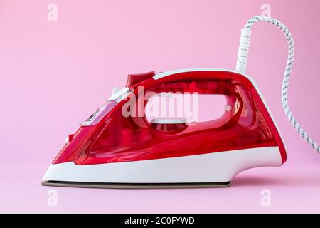 Ferro rosso di plastica su sfondo rosa. Apparecchio per stirare gli abiti, concetto di casalinghi Foto Stock