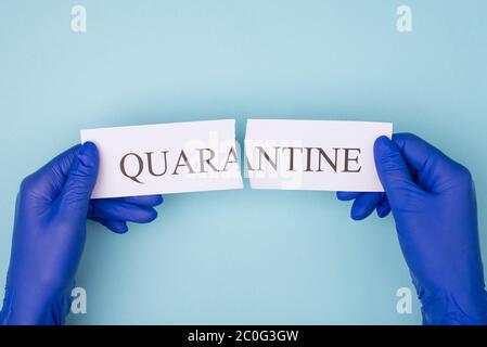 POV primo piano in prima persona sopra l'alto primo piano foto di mani in guanti di gomma che strappano carta con la parola quarantena isolato su sfondo blu Foto Stock