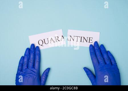 Foto in alto delle mani in guanti posizionate ai lati della parola di quarantena isolata su sfondo blu Foto Stock