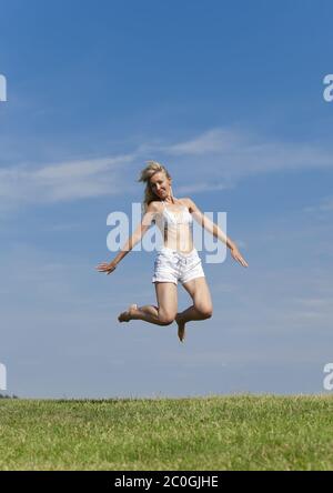 Donna felice in bianco bikini e shorts salta in un Foto Stock