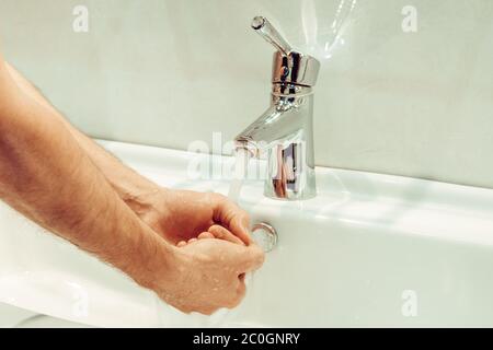 Primo piano di un giovane uomo caucasico che si lava le mani con sapone nel lavello del bagno igiene personale, protezione contro virus e batteri concetto Foto Stock