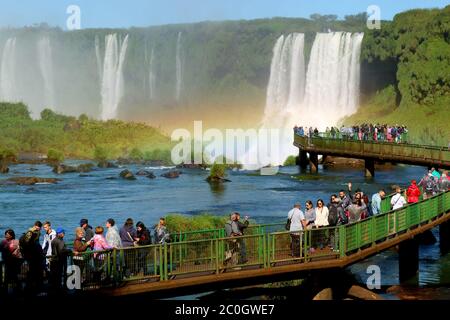 Grande gruppo di visitatori a piedi sulla passeggiata per ammirare le potenti Cascate di Iguazu con un meraviglioso Arcobaleno, Foz do Iguacu, Brasile, Sud America Foto Stock