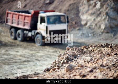 Cumulo di rocce di minerale su sfondo fuori fuoco con camion pesanti carichi multi-ton che esportano minerali da miniera a cielo aperto. Concetto di trasporto Foto Stock