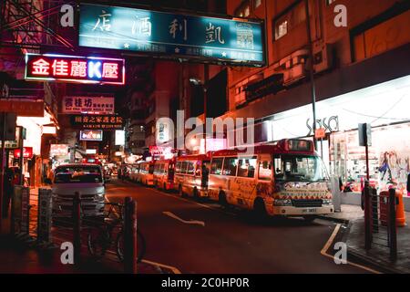 Autobus vuoti che riposano sotto i cartelli al neon in serata su una strada di Hong Kong Foto Stock