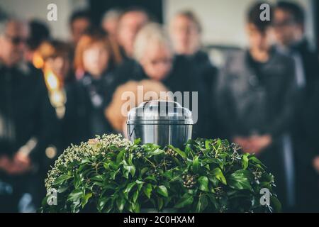 Un'urna metallica con ceneri di un morto su un funerale, con persone che piangono in background su un servizio commemorativo. Triste momento di dolore alla fine di Foto Stock