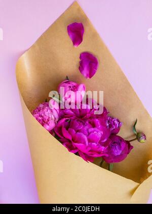 Bouquet di peonie rosa fresche su sfondo rosa avvolto in carta marrone. Consegna fiori. Foto Stock