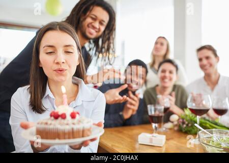 Donna che soffia fuori candela sulla torta al compleanno festa con gli amici a casa Foto Stock