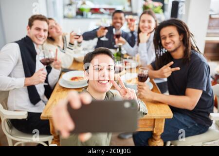 Gli studenti prendono selfie con smartphone mentre mangiano al tavolo di un appartamento condiviso Foto Stock