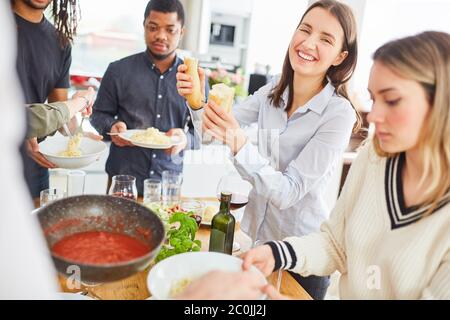 Gruppo di vegani che mangiano insieme in una cucina in comune con spaghetti e salsa di pomodoro Foto Stock