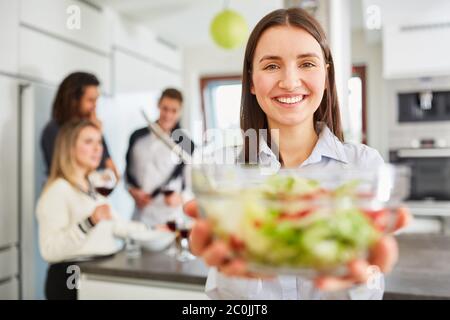 Giovane donna sorridente in cucina con una ciotola di lattuga fresca in entrambe le mani Foto Stock