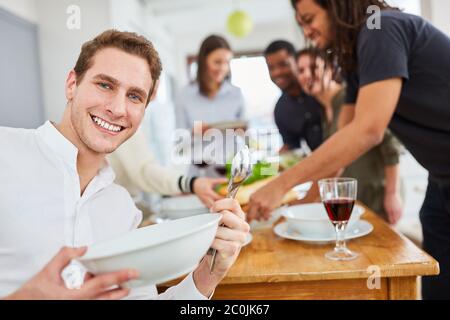Giovane uomo che tiene piatto e cucchiaio mentre si imposta il tavolo in cucina condivisa Foto Stock