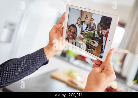 Il gruppo di amici effettua videochiamate in streaming dal vivo utilizzando un tablet mentre si mangia insieme al tavolo Foto Stock