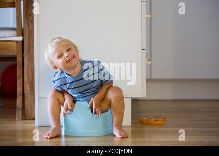 Bambino piccolo, seduto su vasino, giocando con giocattolo di legno a casa Foto Stock