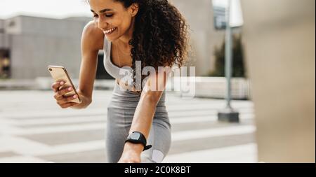 Donna fitness che usa il telefono cellulare mentre si esercita. Donna sorridente che fa allenamento stretching e utilizza il suo smartphone. Foto Stock