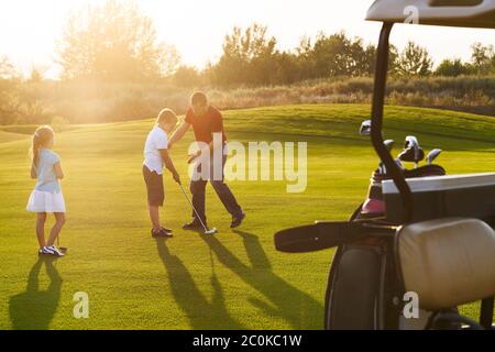 Bambini informali in un campo da golf che tiene i randelli di golf che studing con l'addestratore Foto Stock