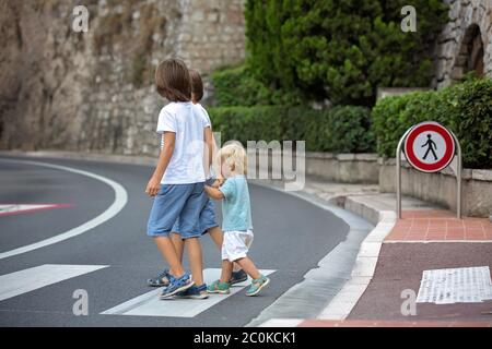 Tre bambini, ragazzi, fratelli, tenendo le mani e attraversando una strada su una passerella a strisce, controllare le auto prima, sicurezza che attraversa la strada sommma Foto Stock