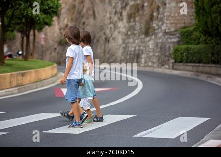 Tre bambini, ragazzi, fratelli, tenendo le mani e attraversando una strada su una passerella a strisce, controllare le auto prima, sicurezza che attraversa la strada sommma Foto Stock