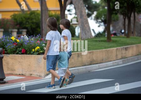 Tre bambini, ragazzi, fratelli, tenendo le mani e attraversando una strada su una passerella a strisce, controllare le auto prima, sicurezza che attraversa la strada sommma Foto Stock