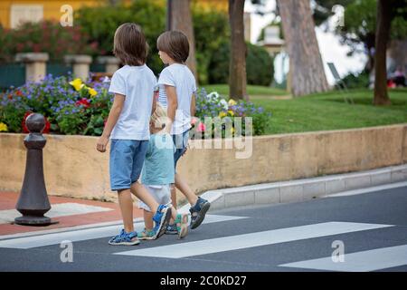 Tre bambini, ragazzi, fratelli, tenendo le mani e attraversando una strada su una passerella a strisce, controllare le auto prima, sicurezza che attraversa la strada sommma Foto Stock