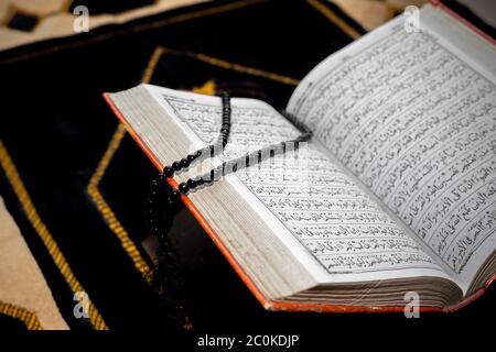 Un aperto il santo Corano con Tasbeeh nero. Il Santo Corano sul tappeto delle preghiere. Focus su font e pagine. Foto Stock
