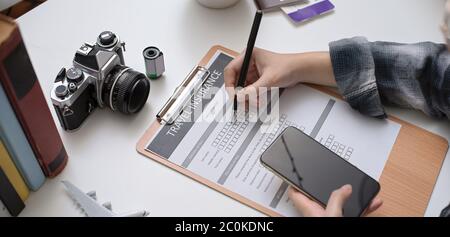 Un'immagine ritagliata del modulo di assicurazione di viaggio per il riempimento femminile mentre guarda il suo piano di viaggio sullo smartphone Foto Stock