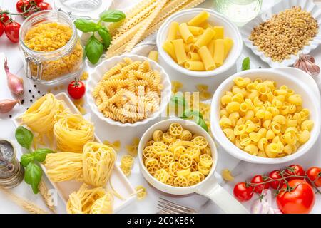 Varietà di tipi e forme di pasta secca - fusilli, penne, nidi di fettuccine, maflaldine, conchiglie, ciotole e ruote - in ciotole bianche con la tradizionale IT Foto Stock