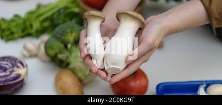 Vista ravvicinata delle mani che tengono i funghi di ostriche mentre si sta a tavola con altre verdure fresche dell'azienda Foto Stock