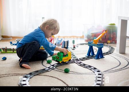 Adorabile ragazzo che gioca con colorati blocchi di plastica a casa, seduto sul pavimento, treno in treno su ferrovia. Giochi creativi per bambini Foto Stock