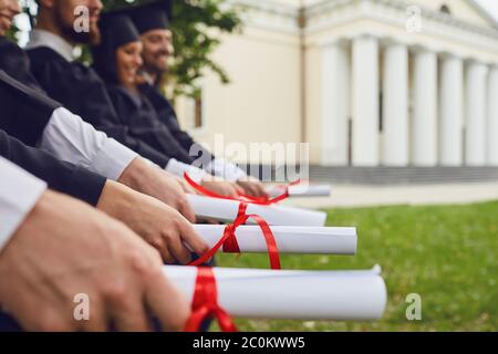 Scroll di diplomi nelle mani di un gruppo di laureati. Foto Stock