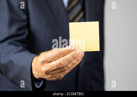 Uomo d'affari in tuta con una nota vuota gialla attaccata davanti a lui. Messa a fuoco selettiva in primo piano. Foto Stock