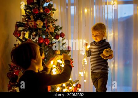 Bel ragazzo biondo, che decorano l'albero di natale con palle e corde di luce a casa Foto Stock