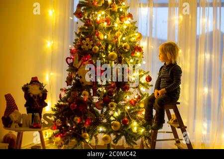 Bel ragazzo biondo, che decorano l'albero di natale con palle e corde di luce a casa Foto Stock